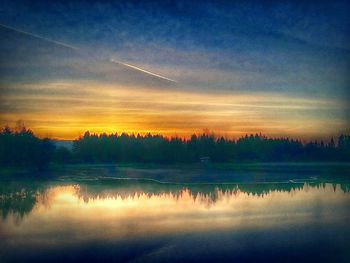 Reflection of trees in lake at sunset