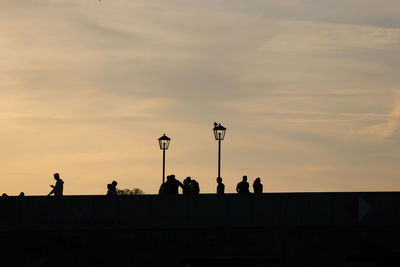 Silhouette people on street against sky at sunset