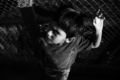 High angle portrait of boy standing by chainlink fence