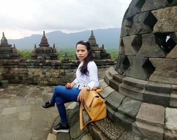 Side view portrait of young woman sitting on stupa at temple