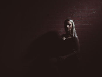 Woman with long hair sitting against wall in darkroom