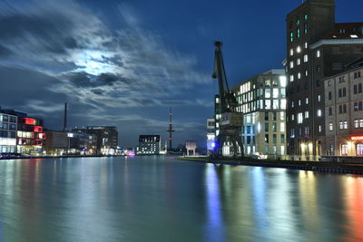 Illuminated buildings by river against sky at night