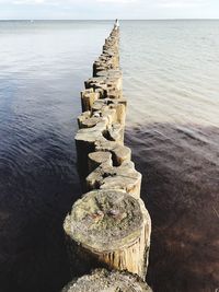 Stack of wooden post in sea against sky
