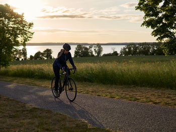 Woman on roadbike riding alongside a field on a lake at evening hour