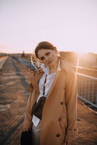 Young woman standing on bridge against sky during sunset