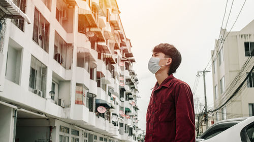 Full length of young man looking away against buildings in city