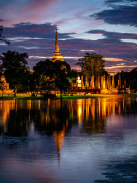 Illuminated building by lake against sky