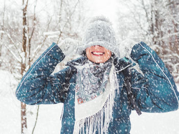 Smiling woman is playing with knitted hat. fun in snowy winter forest. woman laughs.