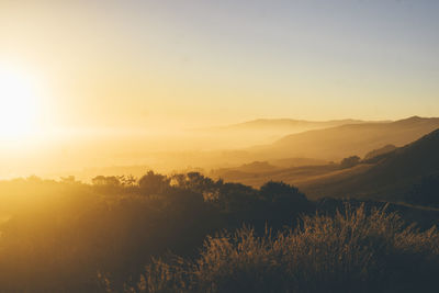 Scenic view of silhouette mountains against sky at sunset over pacific ocean 