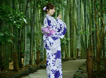 Woman standing by plants against trees 