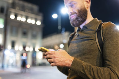 Mature man with beard using mobile phone in city at night