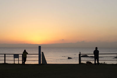 Silhouette people on beach against sky during sunset