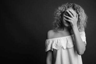 Portrait of woman covering face against black background