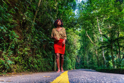 Full length of young man standing by road against trees
