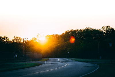 Road by trees against clear sky during sunset