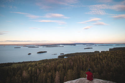 Adventurer sitting on edge of cliff watching lake pielinen in koli national park in eastern finland