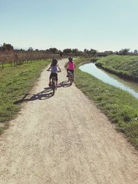 People riding bicycle on field against clear sky