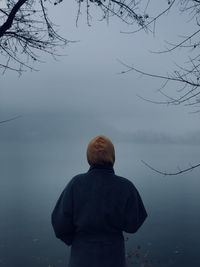 Rear view of a girl standing by the lake in a foggy day