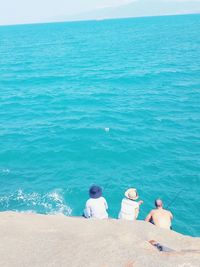 High angle view three men fishing while sitting on rock against sea