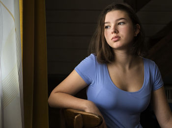Girl looking away while sitting on chair at home