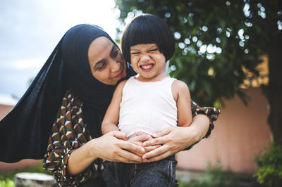 Low angle view of mother embracing playful son in backyard