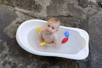 High angle view of cute baby girl sitting in bathtub with toys