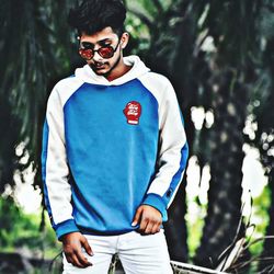 Portrait of young man wearing sunglasses standing against trees