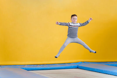 Full length of boy jumping against yellow wall