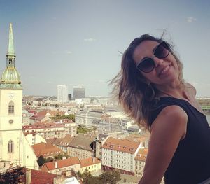 Portrait of beautiful woman standing by buildings in city against sky