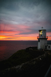 Lighthouse by sea against sky during sunset