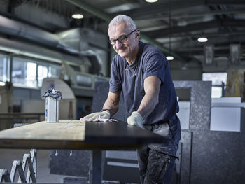 Smiling stonemason polishing stone slab at workshop