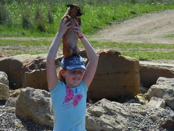 Smiling girl carrying dog while standing on field