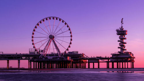 Ferris wheel by pier against sky at sunset