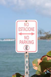 Close-up of no parking sign by sea against sky