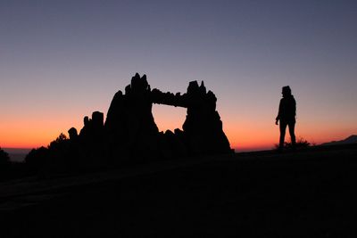 Silhouette of woman standing by rock formation against sky during sunset