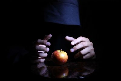 Midsection of person holding apple against black background