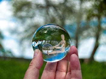 Close-up of hand holding crystal ball with reflection of figurine