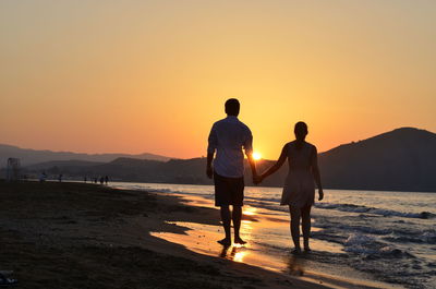 Rear view of silhouette couple standing on shore at beach during sunset