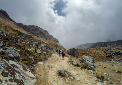 Rear view of hikers walking on mountain against cloudy sky