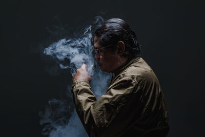 Young man smoking against black background