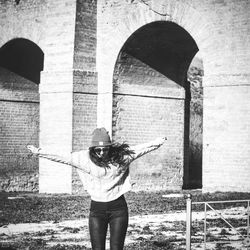 Young woman with arms outstretched standing against old building