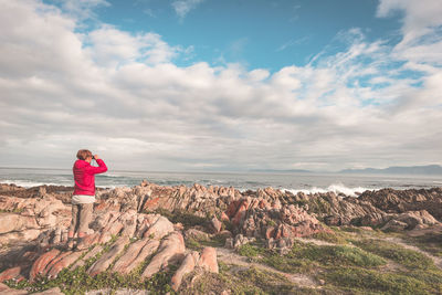 Man standing on rock by sea against sky