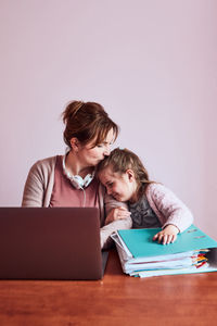 Smiling mother with girl sitting by laptop at home