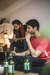 Male soccer fans using mobile phone while watching match at home