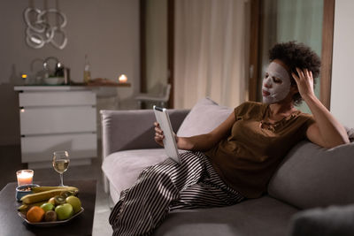 Ethnic woman in sheet mask watching movie