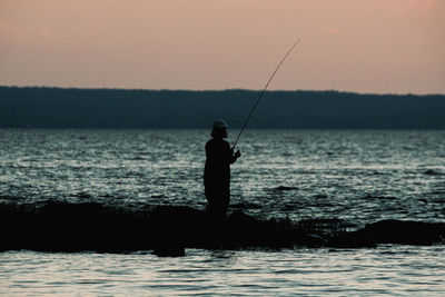 Silhouette man fishing in sea against sky