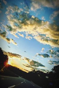 Road by trees against sky during sunset