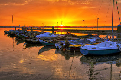 Boats moored in harbor at sunset