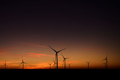 Silhouette wind turbines on land against sky during sunset