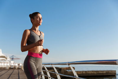 Young woman exercising against clear blue sky